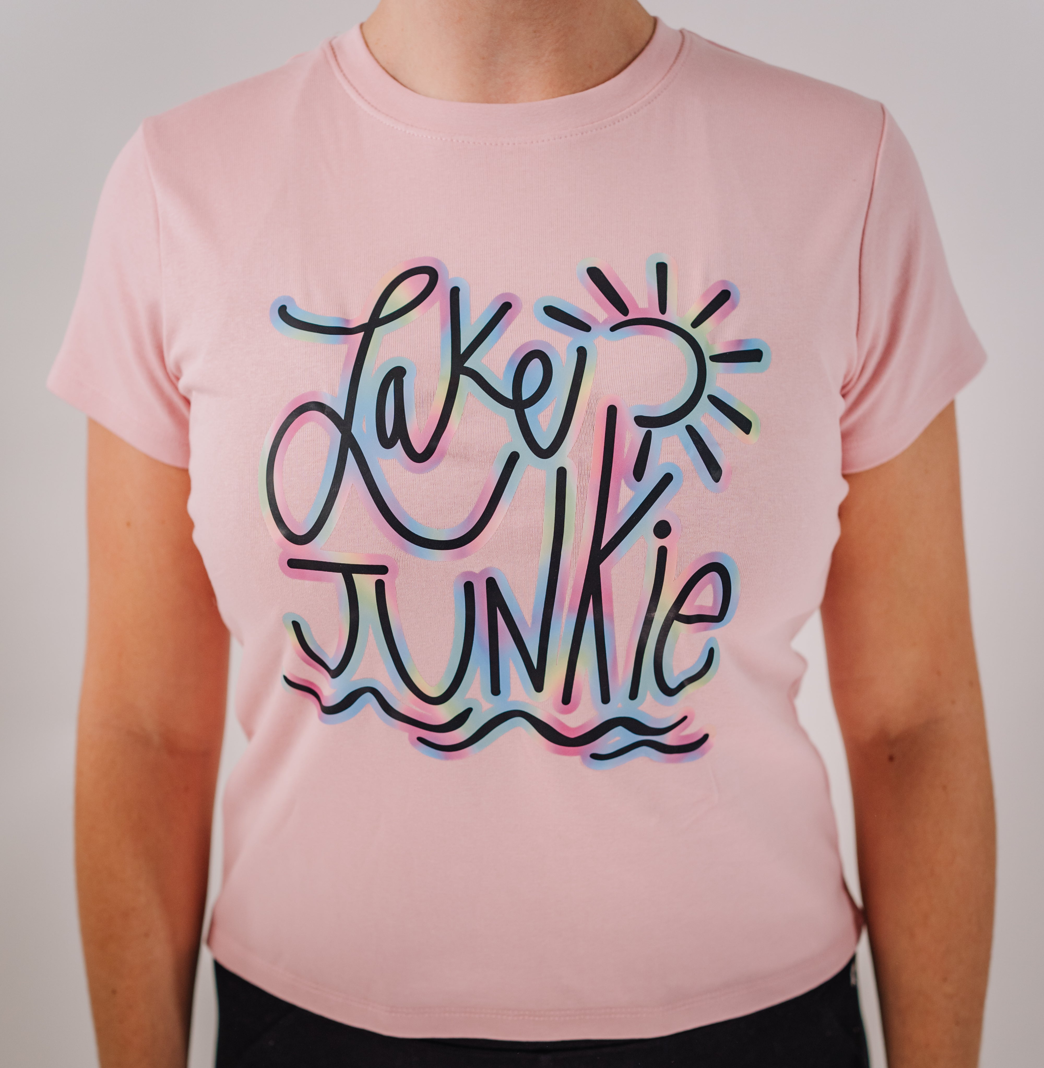 A woman's pink short-sleeve t-shirt with 'LAKE JUNKIE' written in colorful, bold letters on the front.