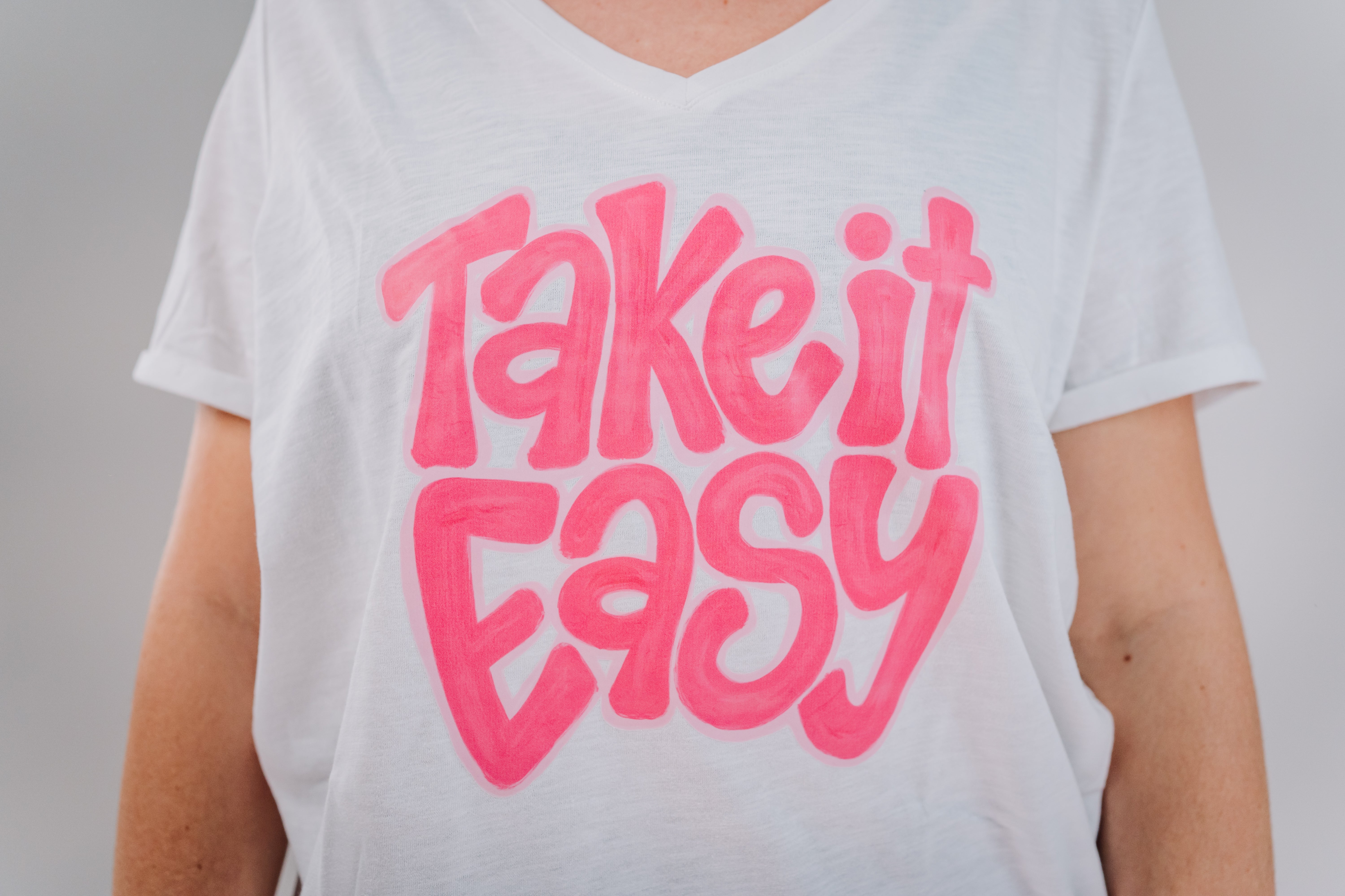 A person wearing a white short-sleeved t-shirt with the text 'Take It Easy' printed in pink.
