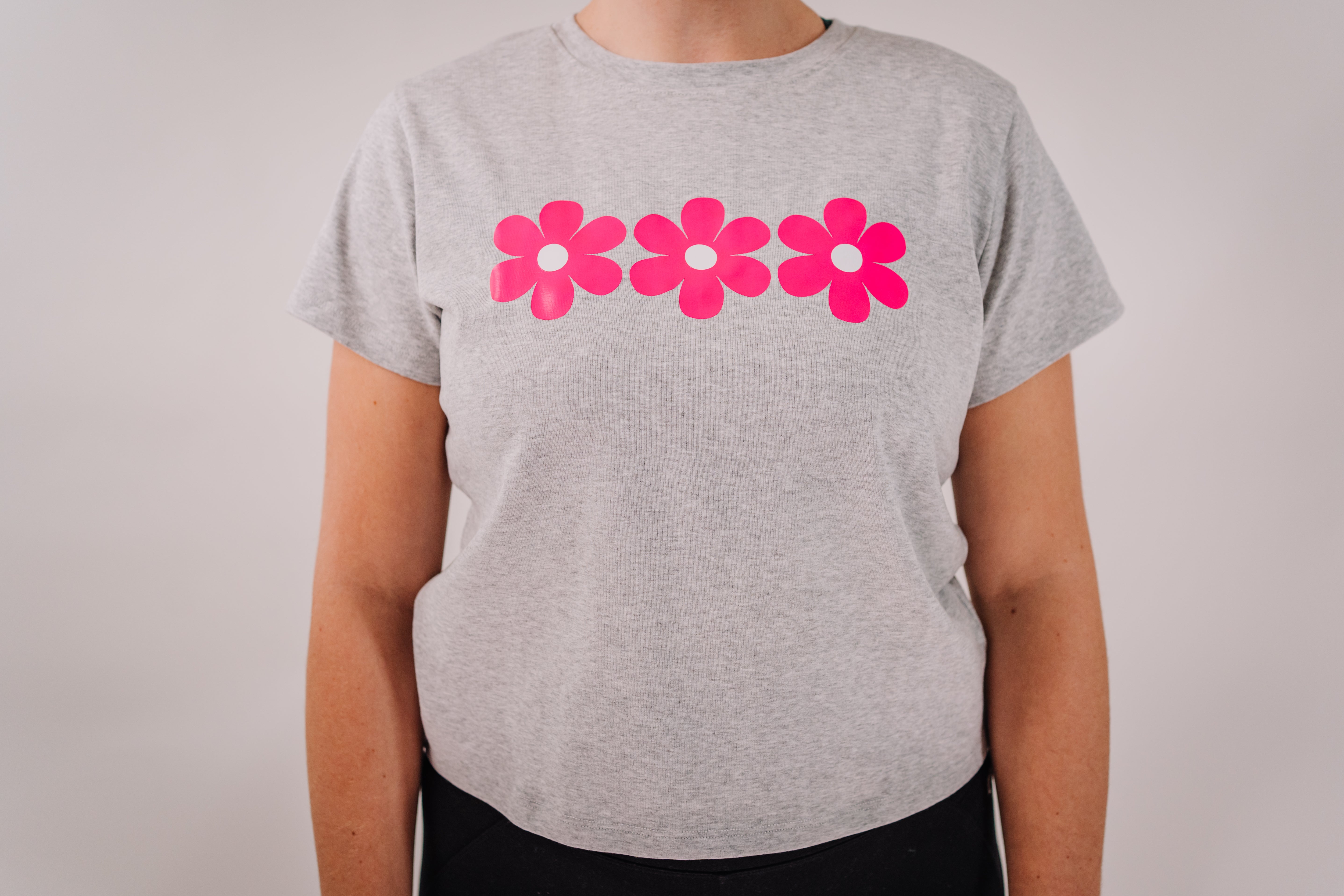 A woman's short sleeve tee shirt in gray with a pink flower design on the chest.