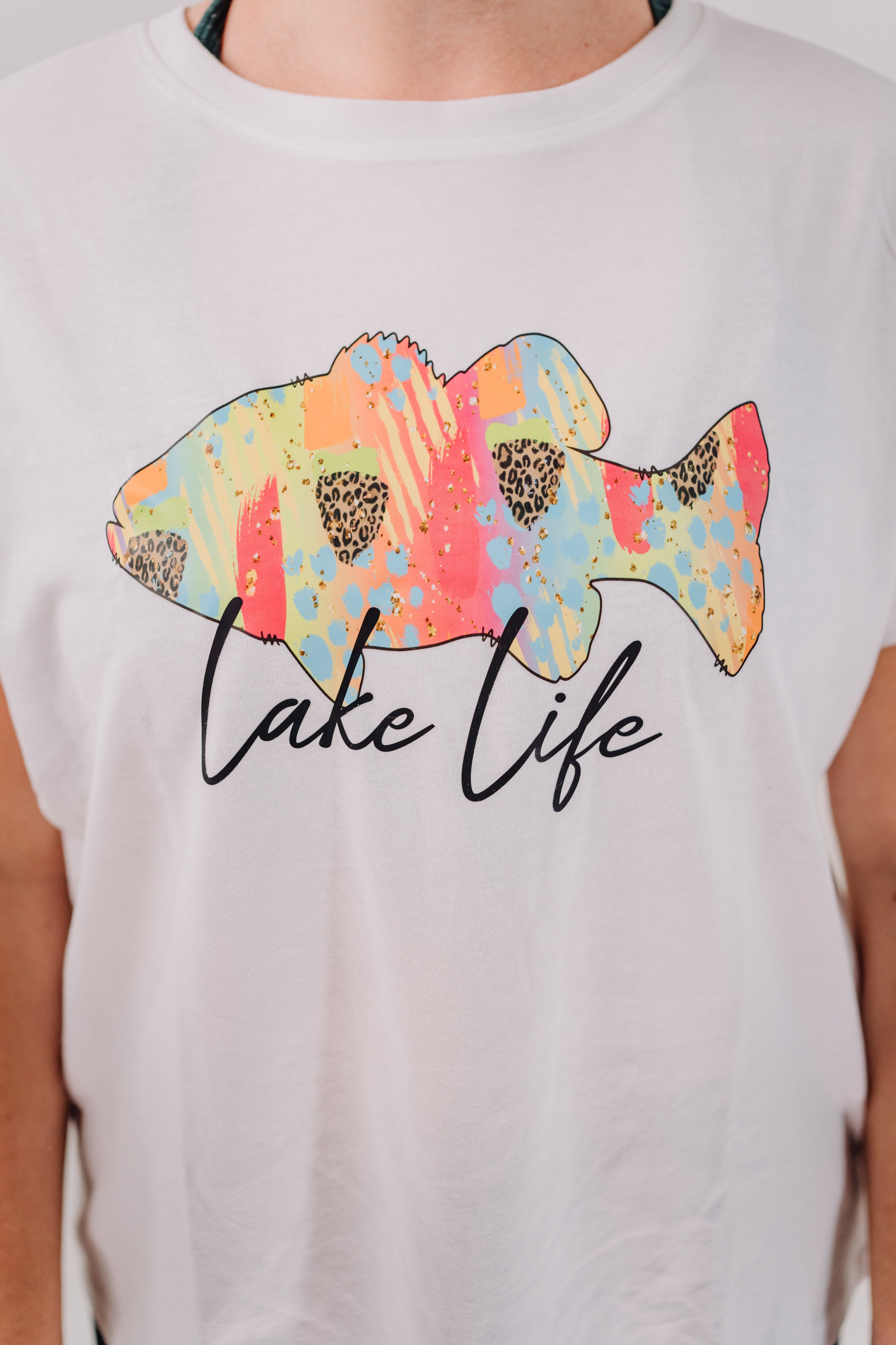 A short-sleeved white t-shirt with a colorful graphic of a trout and the text 'LAKE LIFE' printed on the front.