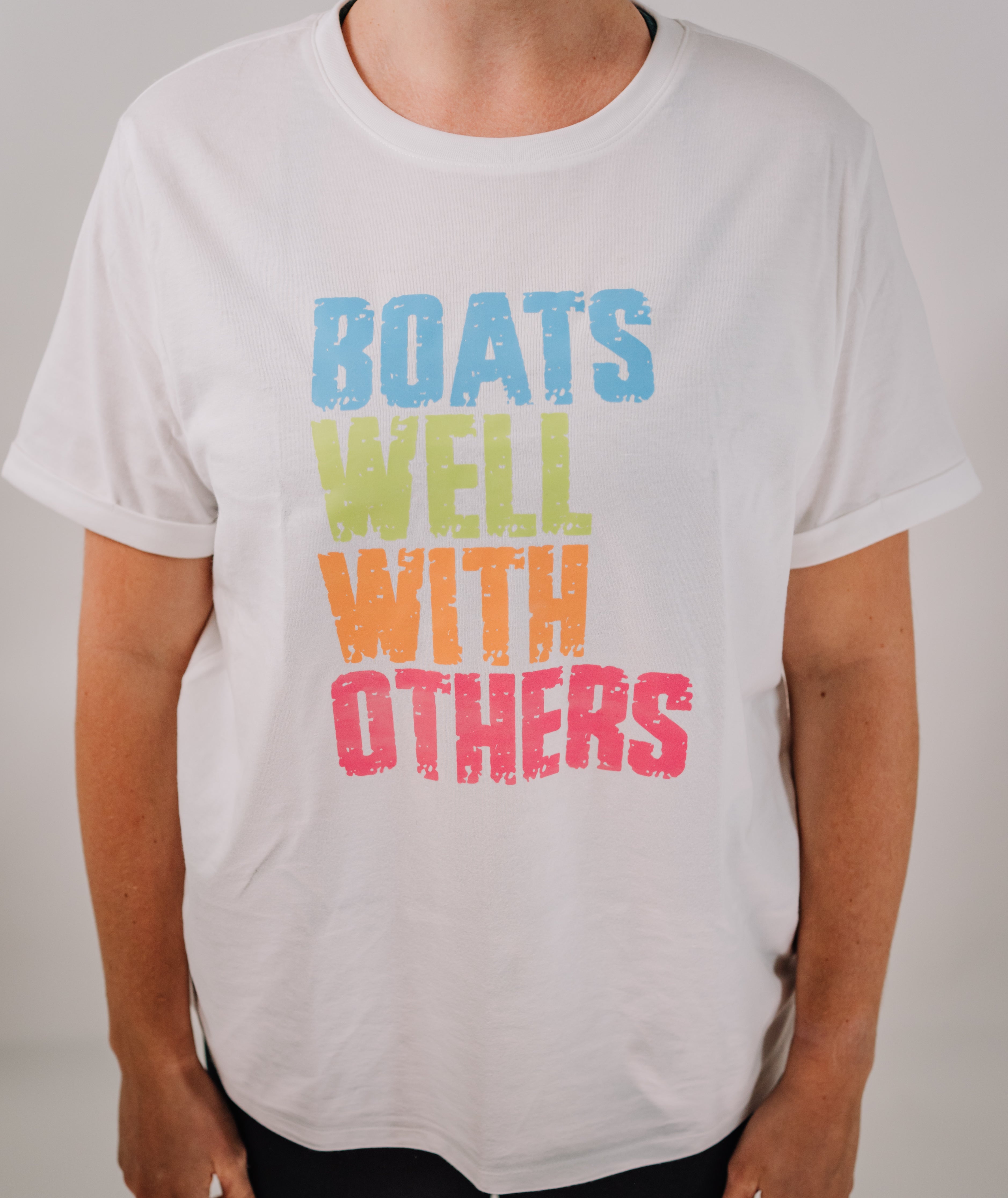 A woman wearing a white short sleeve t-shirt with the text 'BOATS WELL WITH OTHERS' printed on the front.
